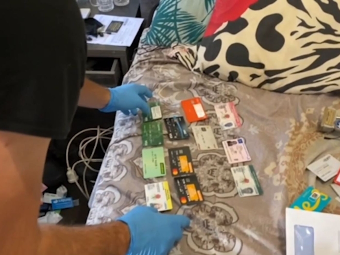 A police officer sorts through assorted identity documents on a bed.