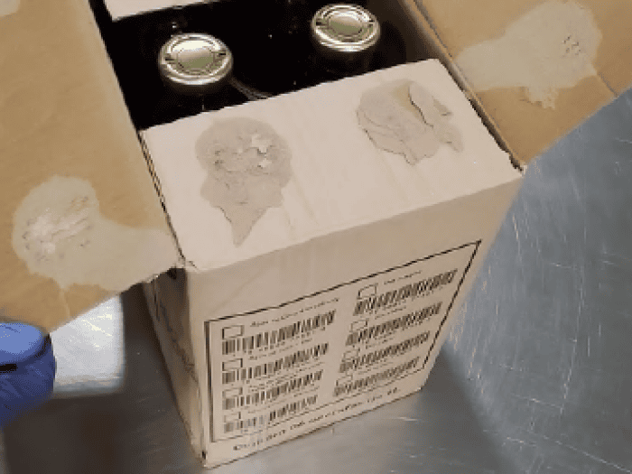 An image of a gloved hand holding a box with juice containers inside