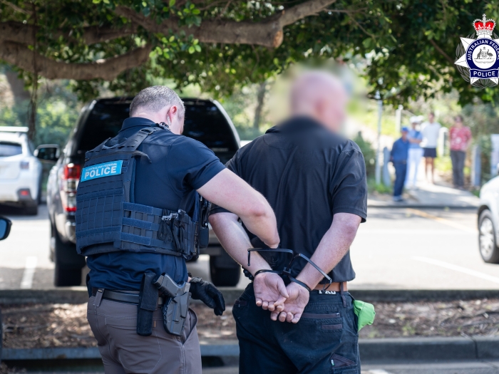 A man in handcuffs whose face is blurred is being held by a police officer 