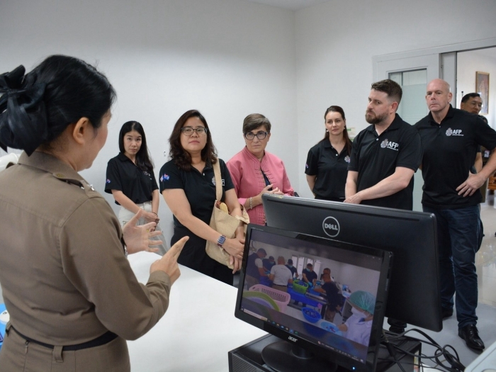 Royal Thai Police scientist standing in front of a computer looking at AFP multiple AFP members who are attending a briefing