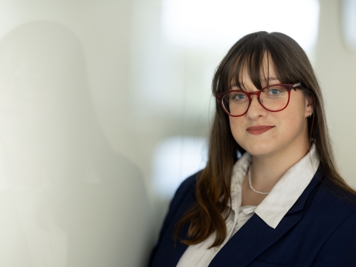 Picture of Elizabeth. She is wearing a blue blazer with a white shirt. She has long brown hair and glasses. 