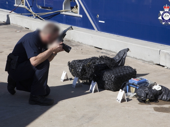 An AFP officer with his face blurred takes a photograph of bags containing a border controlled drug 