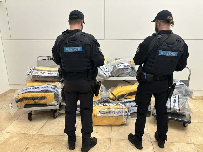 Two officers in uniform standing in front of trolleys loaded with drugs