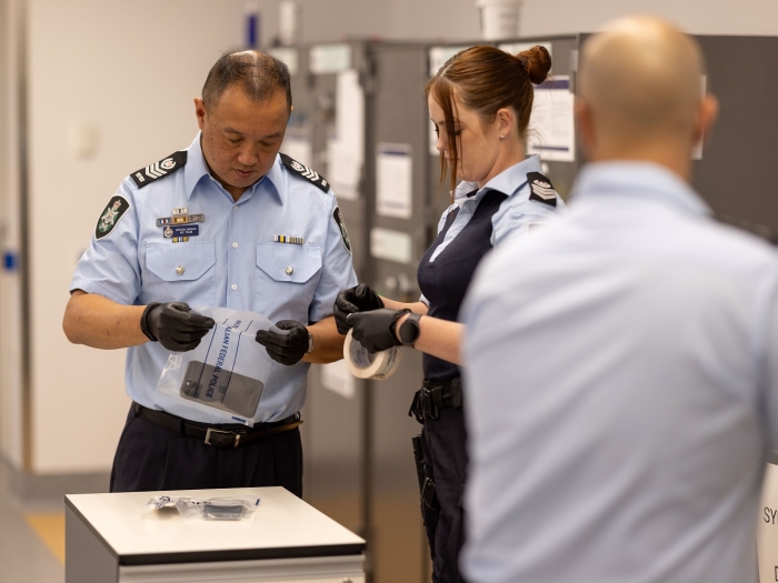 A uniformed police officer with black gloves on, closing a bag with evidence contained