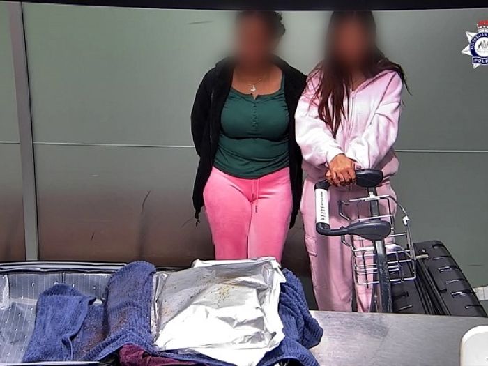 Two women standing behind an open suitcase showing a towel and foil covered in chilli pieces