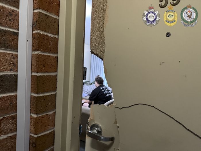 Photo of broken door. Through the hole a man can be seen sitting with his back to the camera