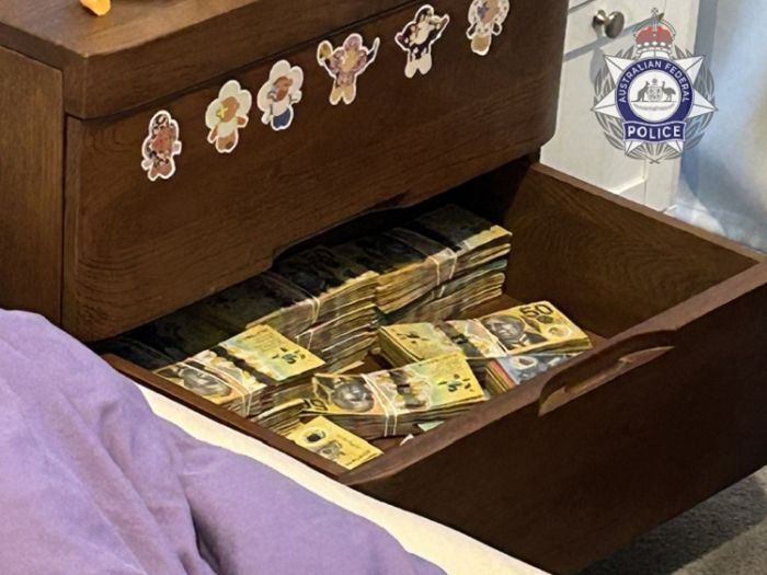 Photo shows a bedside set of draws with one draw filled with bundles of $50 notes