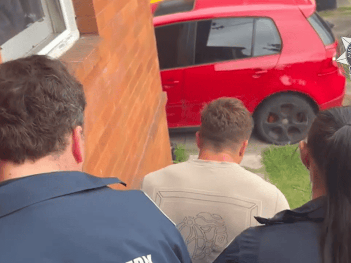 Police offcers walk a man out of a property while under arrest