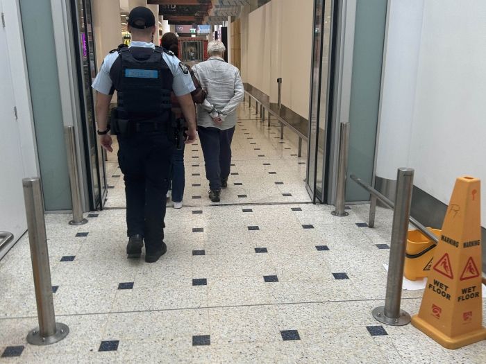 A man is walked through Sydney airport under police custody