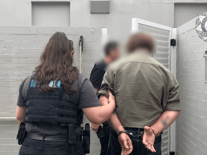 A handcuffed man is walked out of a property by police