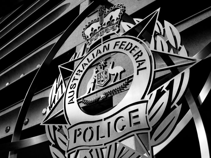 Black-and-white close-up of the Australian Federal Police emblem outside a building.
