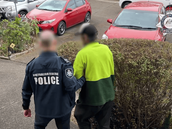 AFP officer walks alleged offender out of house and into police car