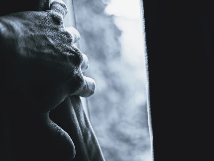 Image of a hand pushing a curtain aside to view through a window
