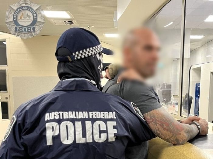 A man in a grey shirt is restrained by AFP officers.