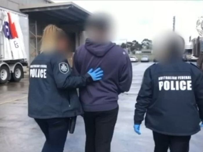 A man in a navy blue hoodie is escorted by two police officers.