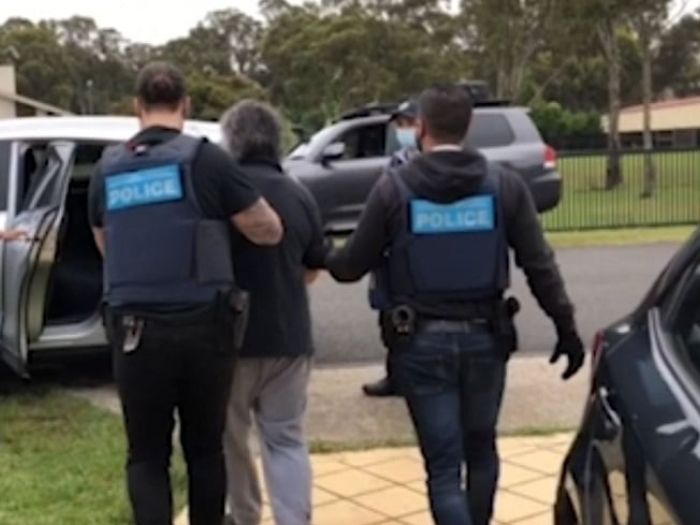 A man in a black shirt is led to a car by two police officers.