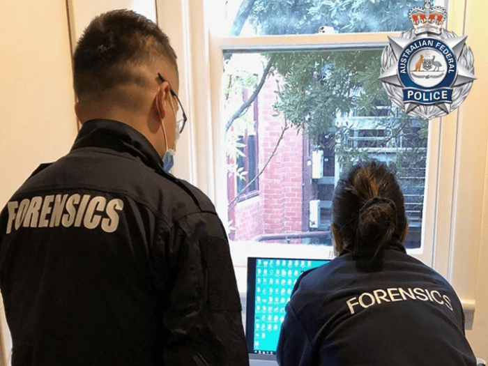 Two AFP forensic scientists stand at a desk looking at a computer screen