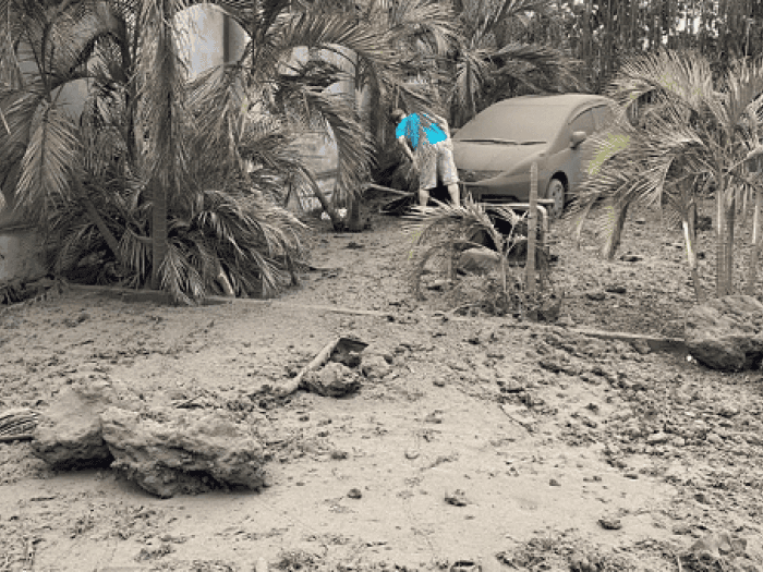 A man in a blue shirt inspects a vehicle covered in volcanic ash