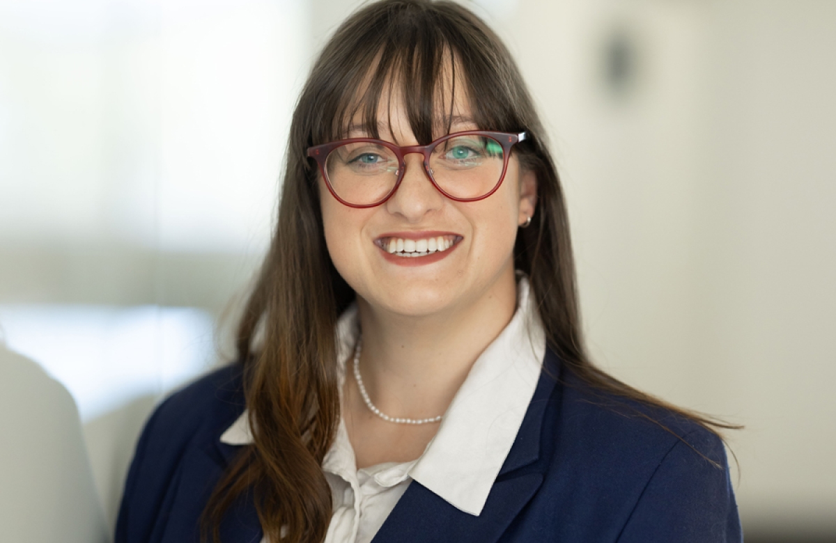 Portrait of Elizabeth. She is wearing a navy blue blazer and white shirt and has long brown hair and glasses. 