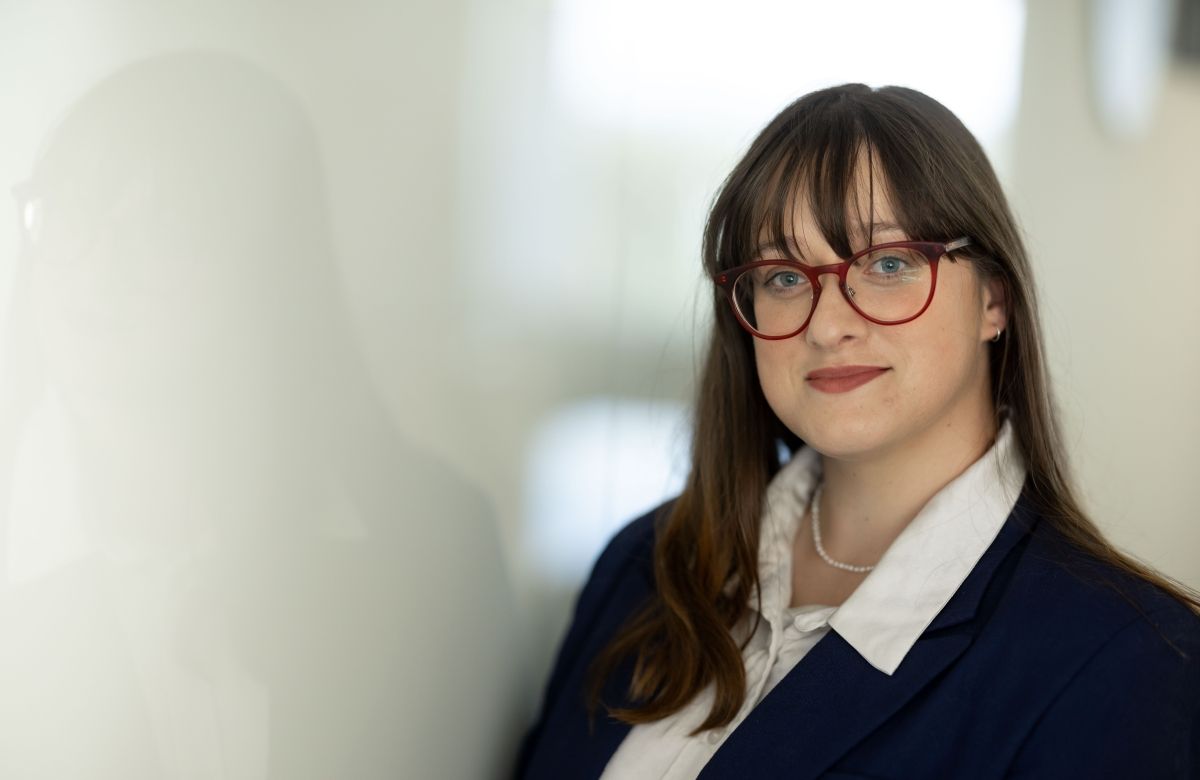 Picture of Elizabeth. She is wearing a blue blazer with a white shirt. She has long brown hair and glasses. 
