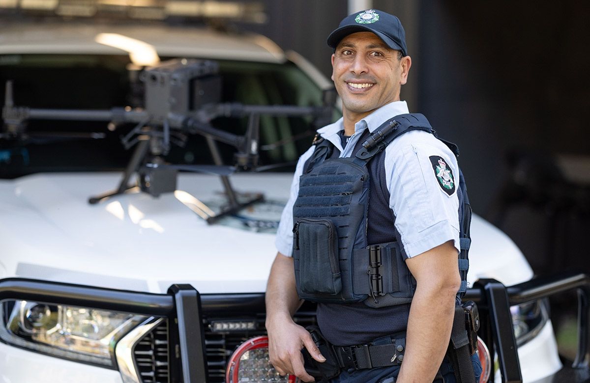 A uniformed office, with a drone on the bonnet of a white police vehicle behind him