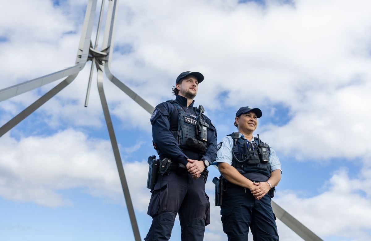 Two protective service officers on the grass at Parliament House with the flag behind them