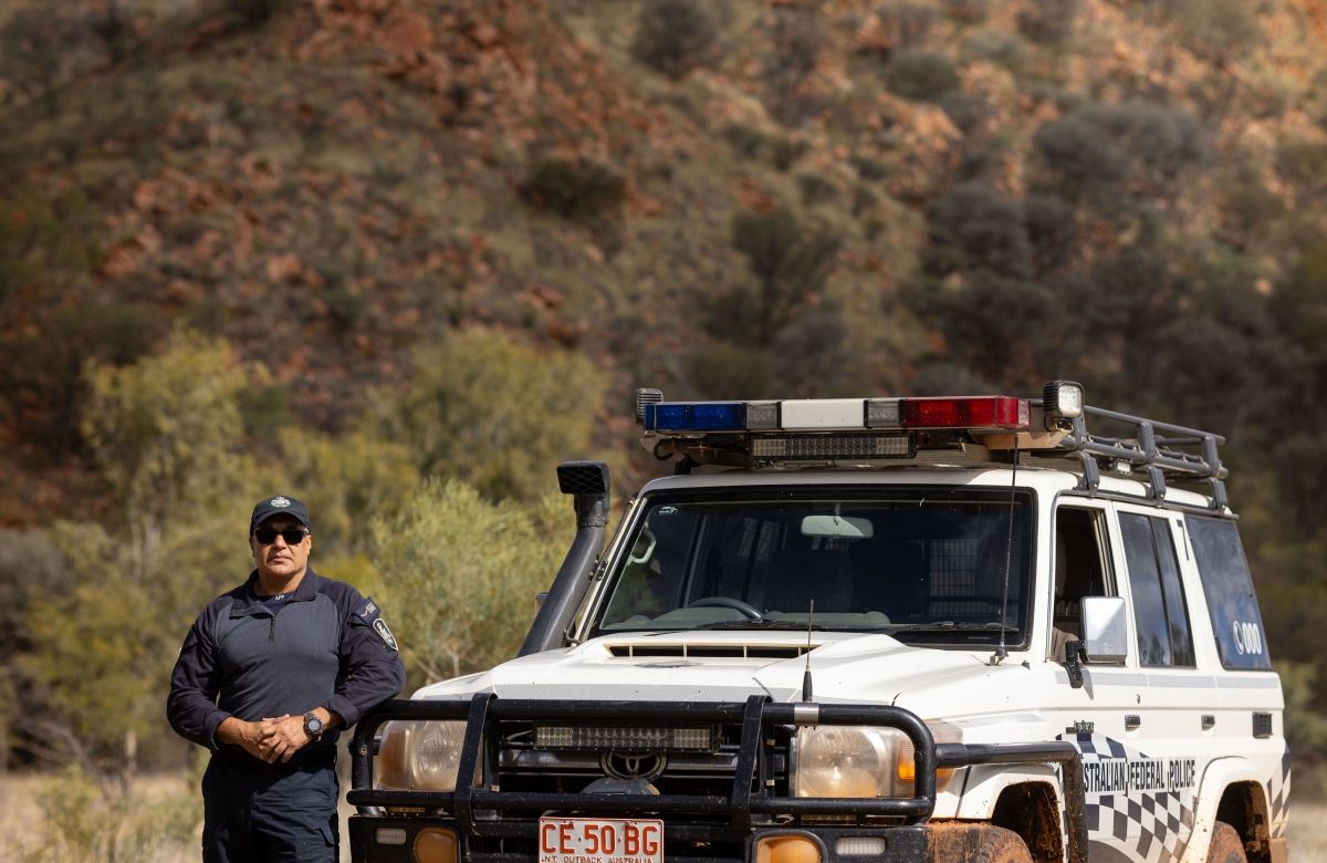 Protective Service Officer leaning against AFP Four wheel drive with Australian outback behind him