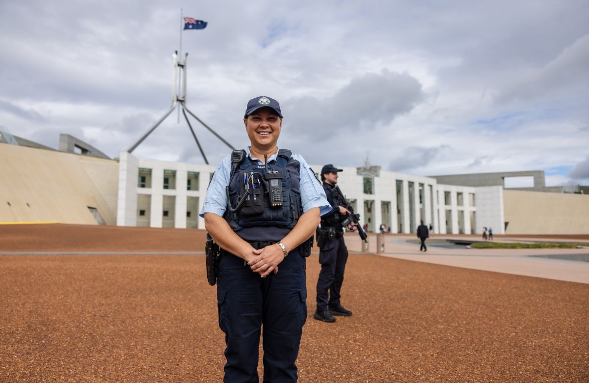 A Protective Service Officer (PSO) stands in front of the Australian Parliament House with another officer behind her