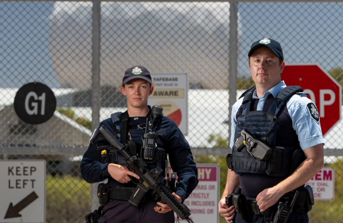 Two armed AFP Protective Service Officers standing outside a security date with a satellite behind 