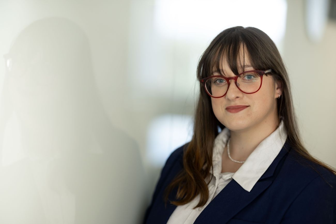 Picture of Elizabeth. She is wearing a blue blazer with a white shirt. She has long brown hair and glasses. 