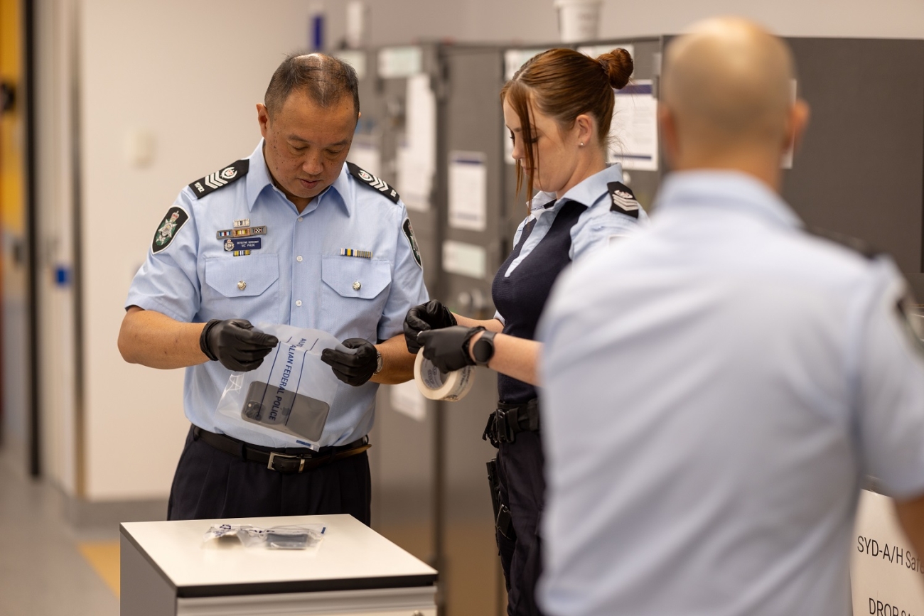 A uniformed police officer with black gloves on, closing a bag with evidence contained