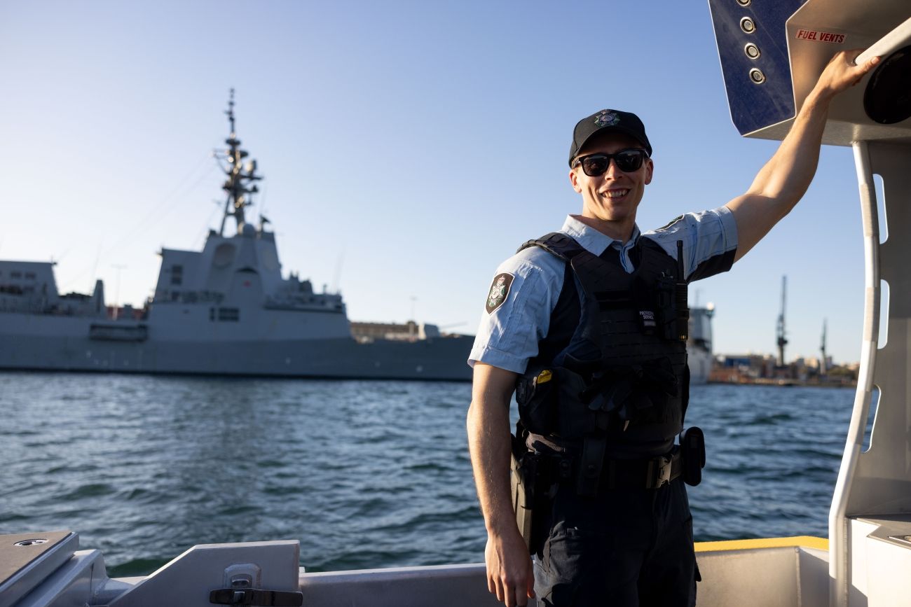 Protective Service Officer on a boat in Sydney Harbour with a large naval behind him