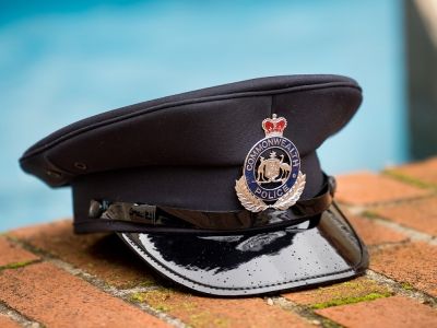 A dark navy Commonwealth Police cap resting on a brick surface, with the official badge and crown emblem visible on the front.