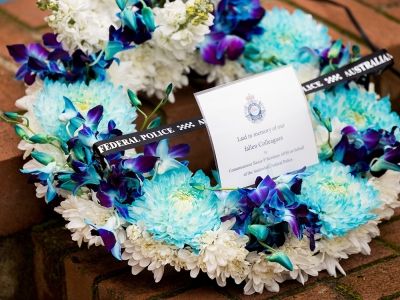 A floral memorial wreath in blue and white with a remembrance card and ribbon, placed on brick paving.